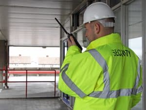 A construction site security guard patrols the site with a radio in one hand