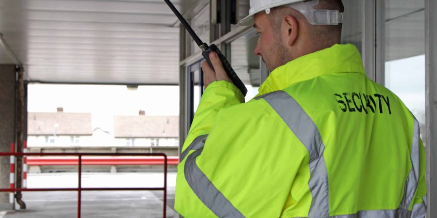 A construction site security guard patrols the site with a radio in one hand